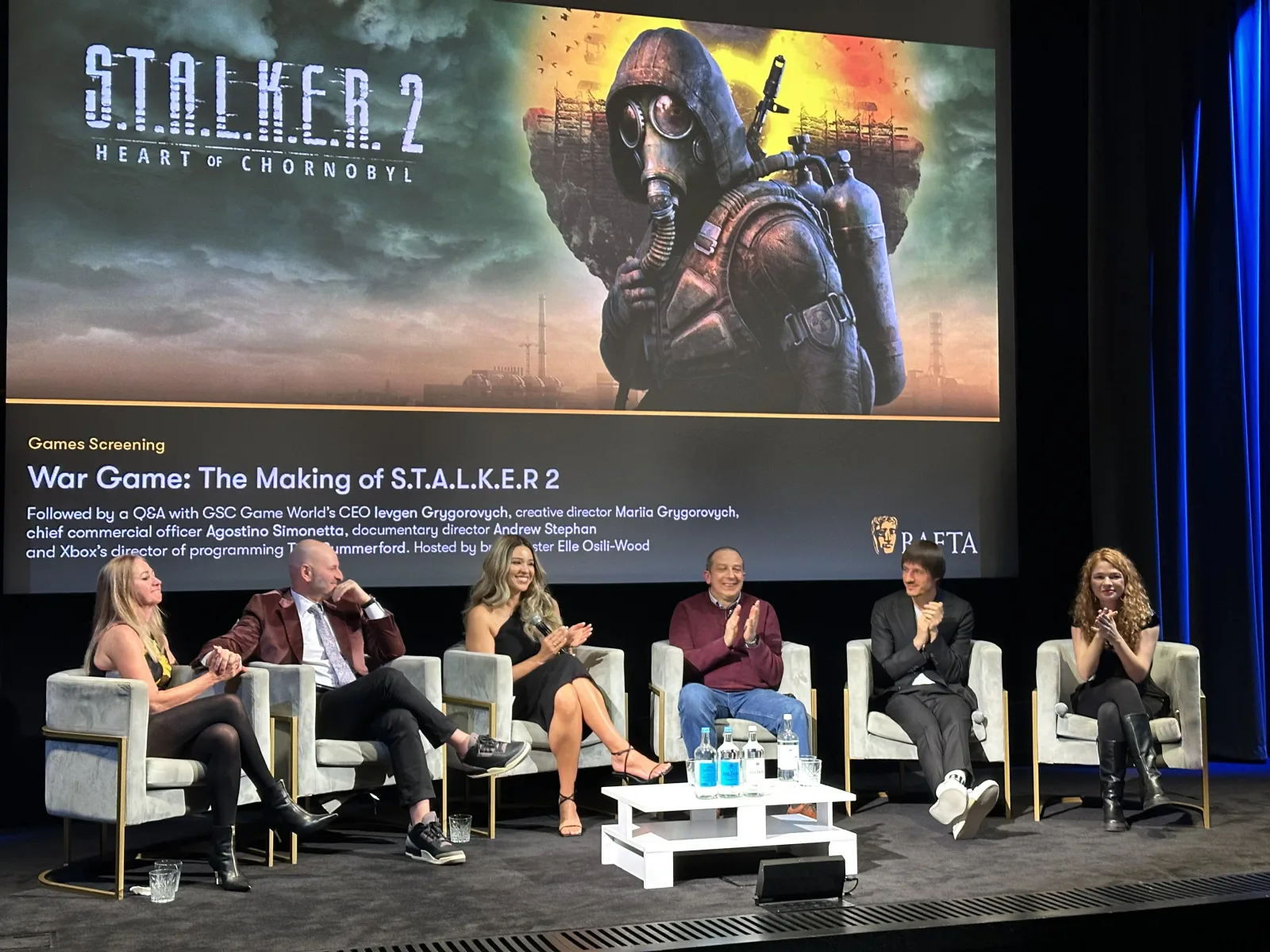 A panel on stage in front of a large screen showing S.T.A.L.K.E.R. 2 key art, at a screening of the documentary War Game: The Making of S.T.A.L.K.E.R. 2.